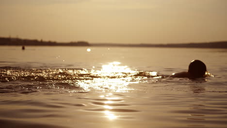 boys are diving in the evening river at sunset. silhouette of two kids swim under water in the evening during summer holidays.