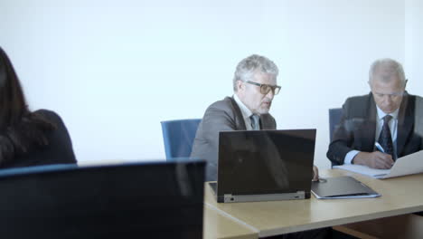 mature male business leader meeting with partner and businesswoman using computer with data