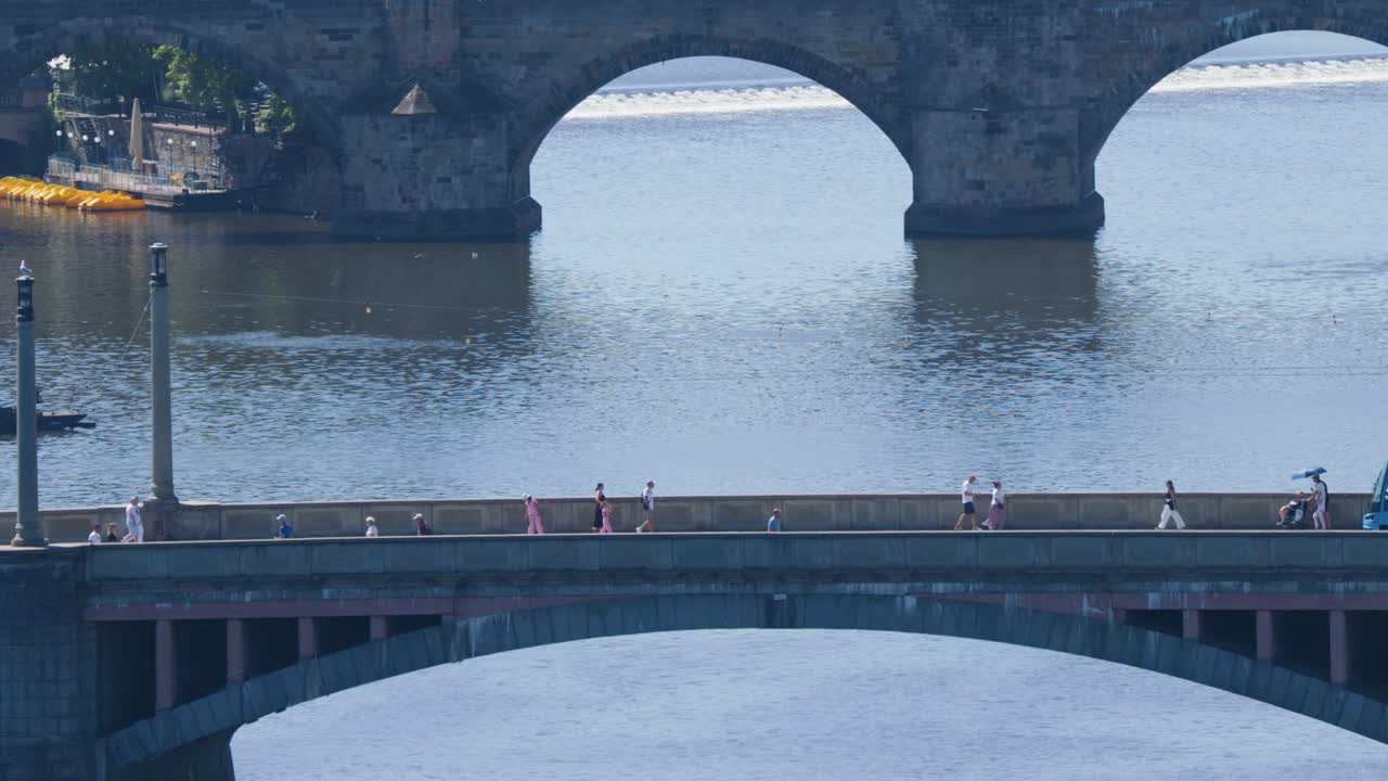 Blue tram travels across bridge above Vltava River, historic Prague bridges, sunny summer daylight