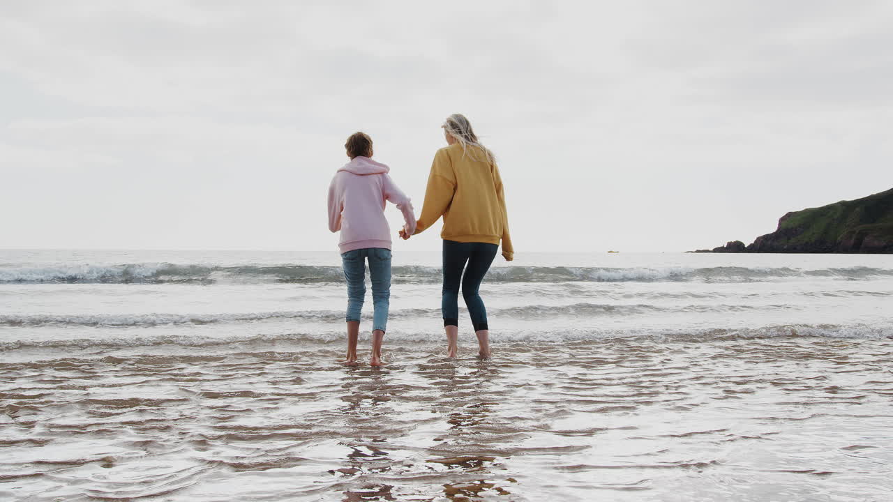 엄마와 딸이 가을 해변 휴가에서 파도를 뛰어넘고 있습니다.