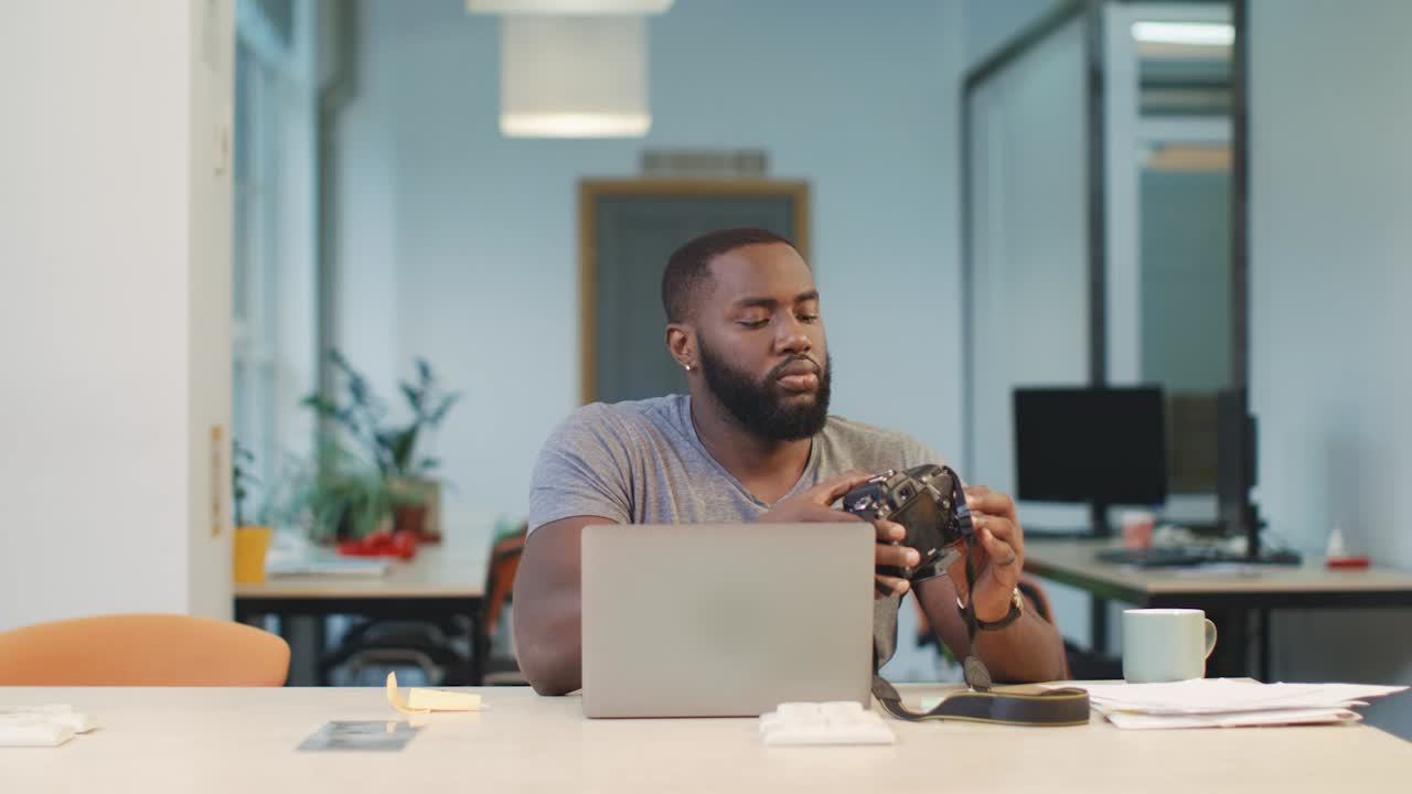 Uomo africano che collega la fotocamera al notebook. Uomo che carica le foto sul computer