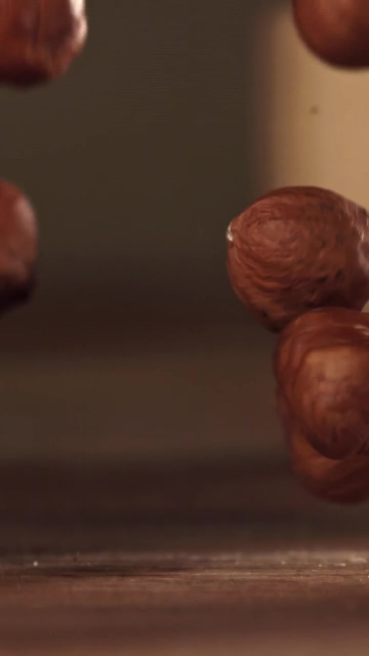Nocciole sgusciate che cadono al rallentatore su una superficie di legno.