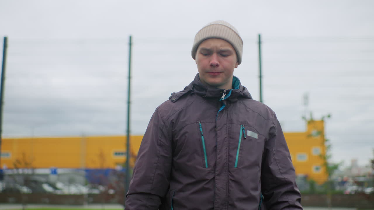 caucasian man dribbles basketball outdoors wearing beanie and jacket on overcast urban court practicing bounce and pass pausing in reflective pose casual street sport training cool autumn tones