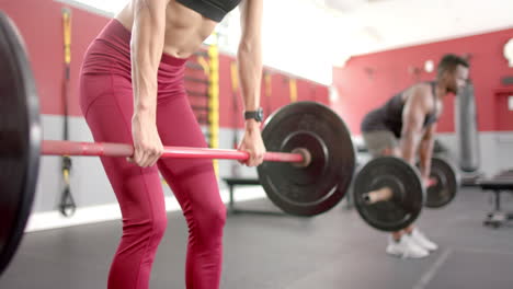 joven mujer blanca en forma y hombre afroamericano en el gimnasio levantando pesas