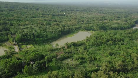 Aerial-flight-over-lake-result-of-volcanic-sand-mining-surrounded-by-green-jungle-of-Indonesia-during-sunny-day-misty-day