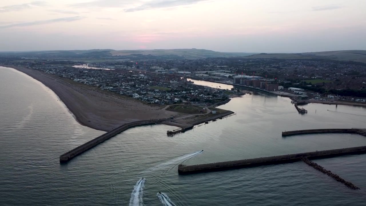 Vista aérea de drone de jet skis navegando para um porto de uma cidade costeira ao entardecer.