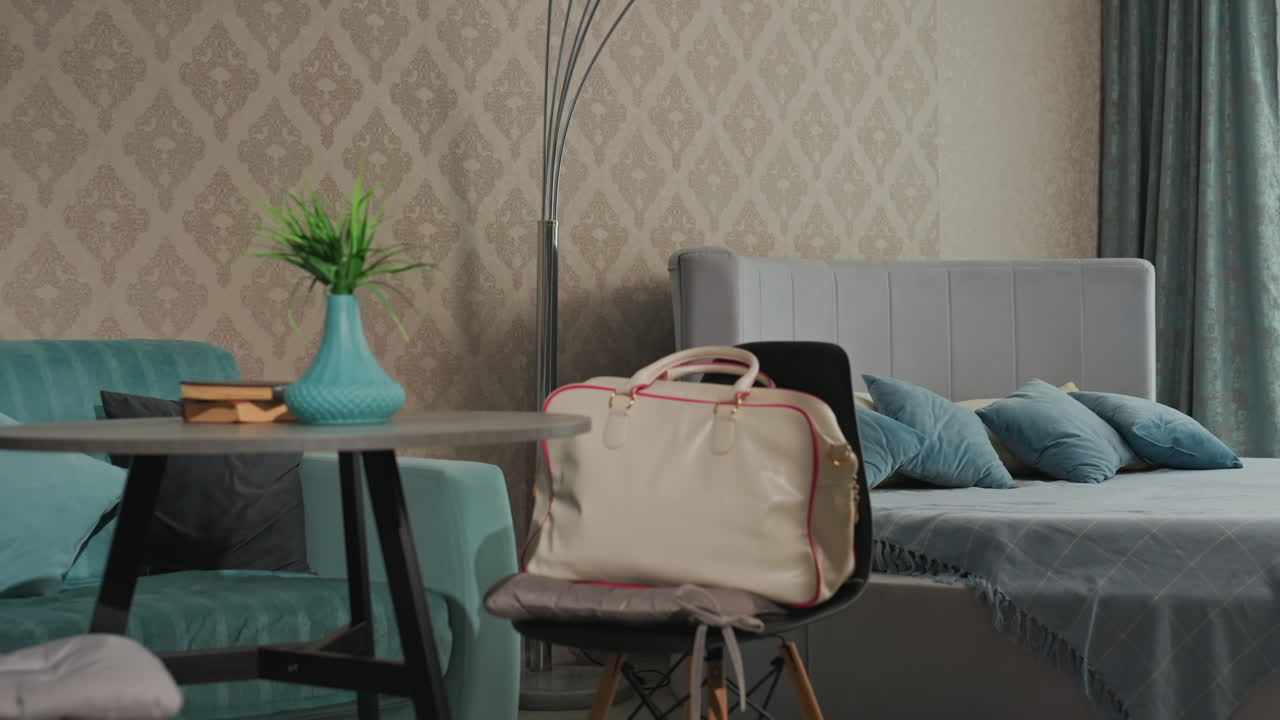 modern bedroom with upholstered bed and velvet pillows against patterned wallpaper, arched floor lamp providing ambient light, teal curtains framing window, decorative plant in vase and bag on chair