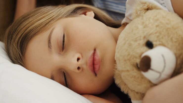 Close-up view of cute blonde little girl sleeping on the bed while hugging her teddy bear in the morning