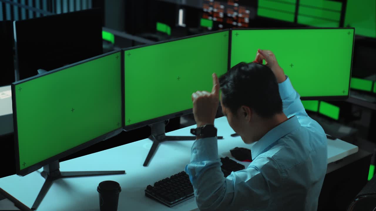 seitenansicht eines glücklichen asiatischen mannes, der feiert und tanzt, während er mit mehreren computermonitoren im büro arbeitet