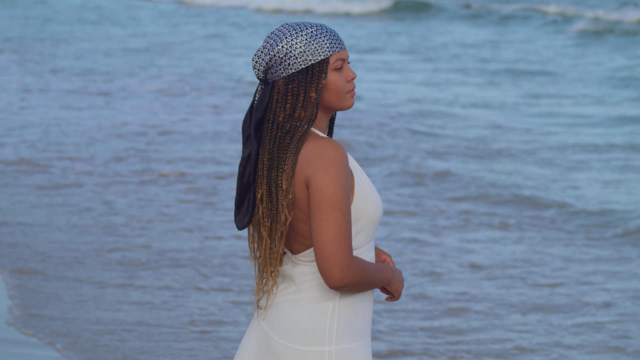 vista de cámara descendente de una mujer joven parada en la playa con un vestido de playa mirando el cielo azul en el fondo