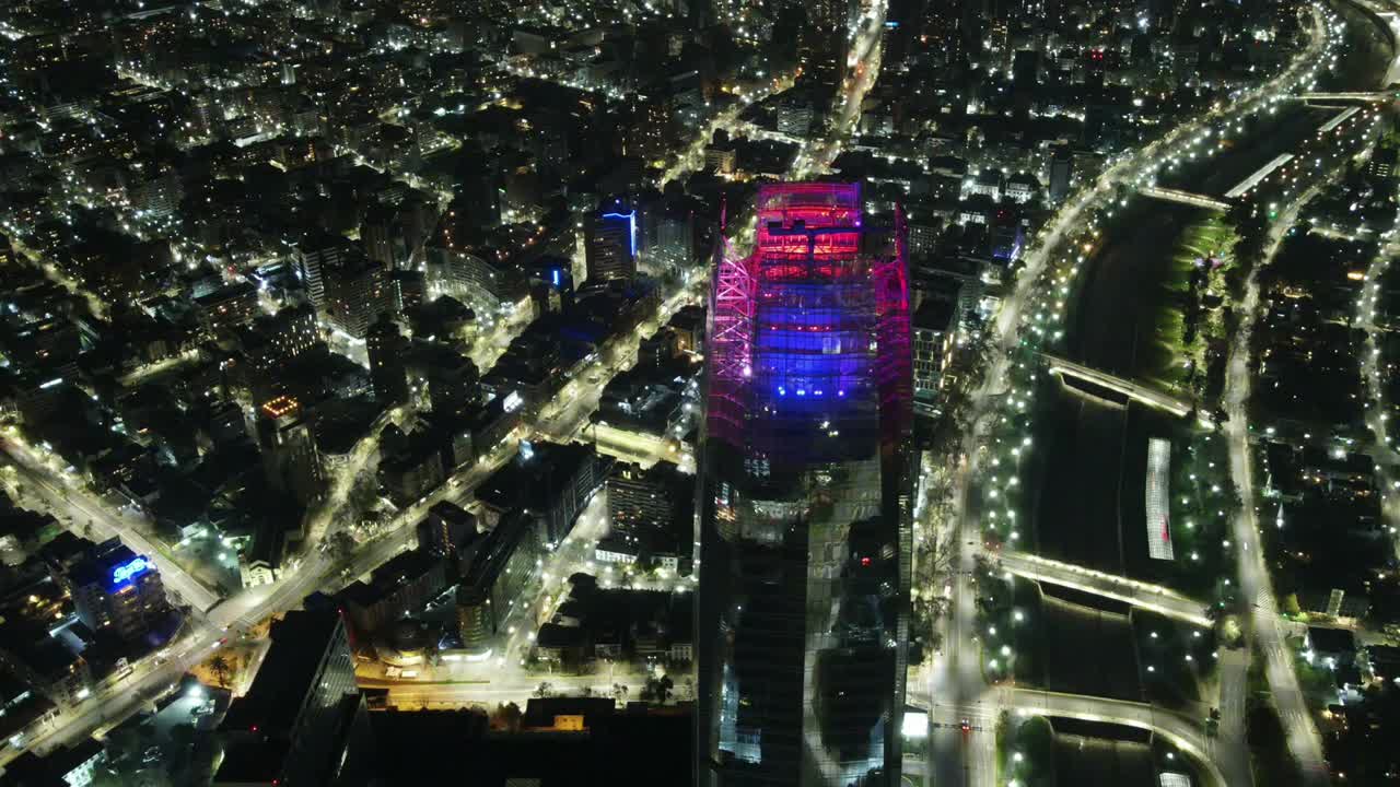 Cinematic aerial drone night view of the illuminated Costanera Center skyscraper (Gran Torre Santiago) towering over the city lights and Mapocho River in Santiago, Chile, 4K