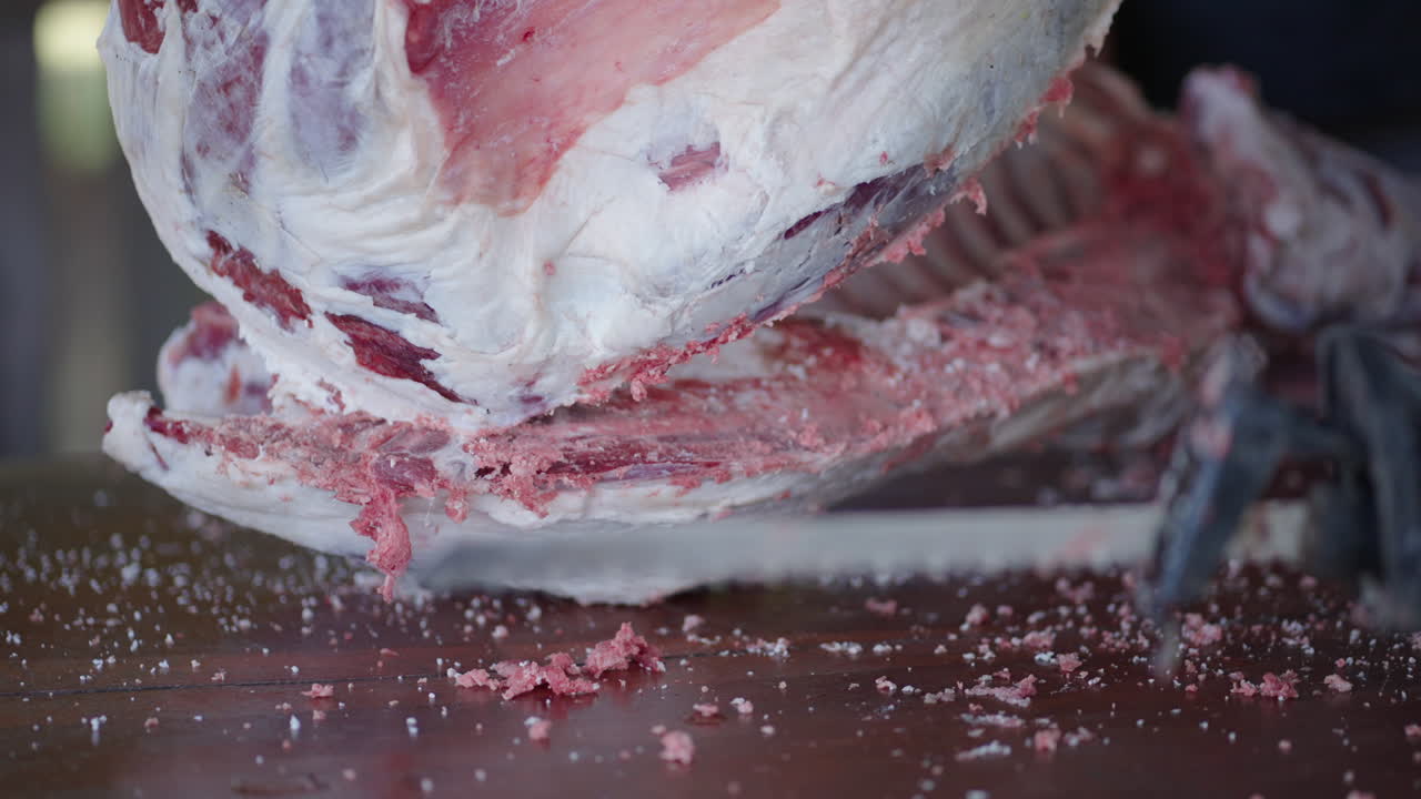 un primer plano de un hombre trabajando en un carnicero cortando carne de cordero con una sierra eléctrica.