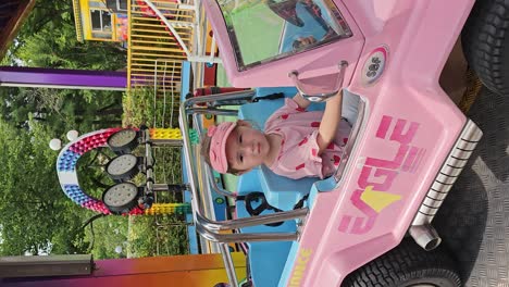 seoul land amusement park -scary toddler girl waves hand sitting in colorful car roller coaster getting ready for ride - vertical