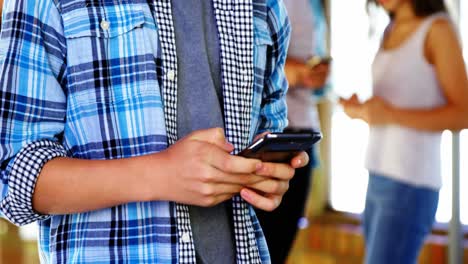 Mid-section-of-boy-using-mobile-phone-in-corridor