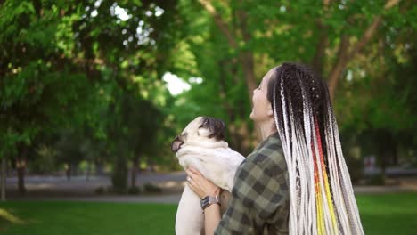 the girl and pug dog are having fun, dreadlocks woman throws the dog in the air in the park