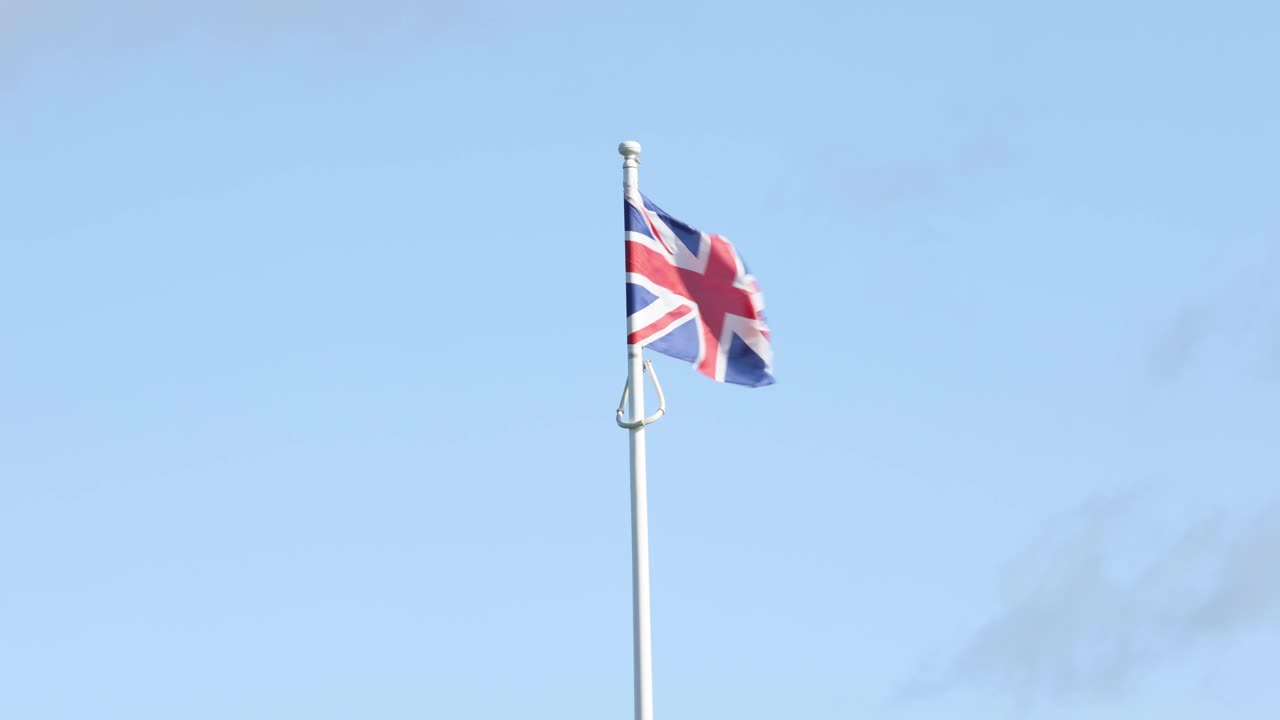 Håndholdt optagelse af et Union Jack flag, der blafrer i vinden på en flagstang.