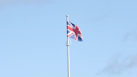 hand-held shot of a union jack flag flying in thew wind on a pole