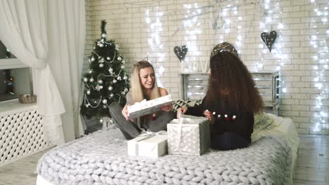 women with christmas gift boxes. lovely attractive girls holding christmas gifts while sitting on bed