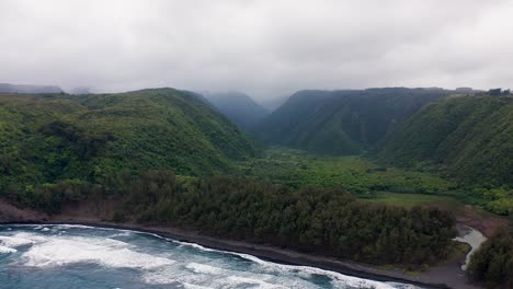 powerful waves crash along a rugged shoreline beneath towering green cliffs, while a misty valley opens beyond, framed by steep slopes and dense forest in this dramatic coastal landscape.