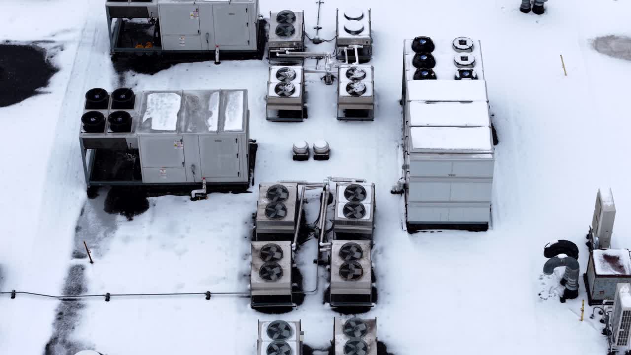 Snow-covered HVAC units on a rooftop, captured in winter, evoke chill