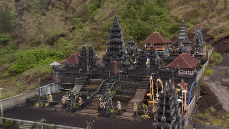 Aufsteigende-Luftaufnahme-Von-Atemberaubenden-Schwarzen-Steinsäulen-Und-Farbenfrohen-Statuen-Im-Hindu-tempel-Pura-Pasar-Agung-Auf-Der-Seite-Des-Berges-Agung-In-Bali