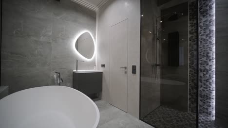 een ruime badkamerontwerp met een slanke vrijstaande badkuip, een verlichte spiegel en een walk-in douche met gedetailleerd tegelwerk