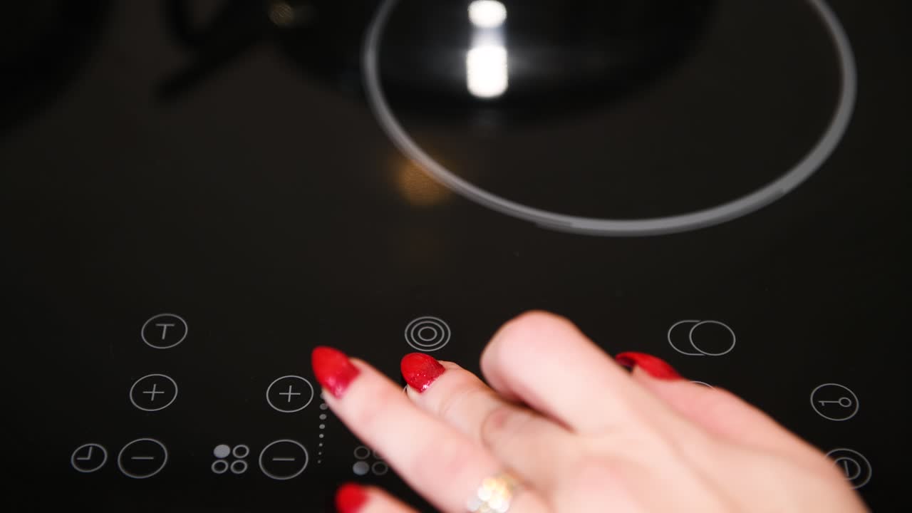 Female finger operating electric stove, nicely manicured finger nails, red polish, LED indicators illuminated