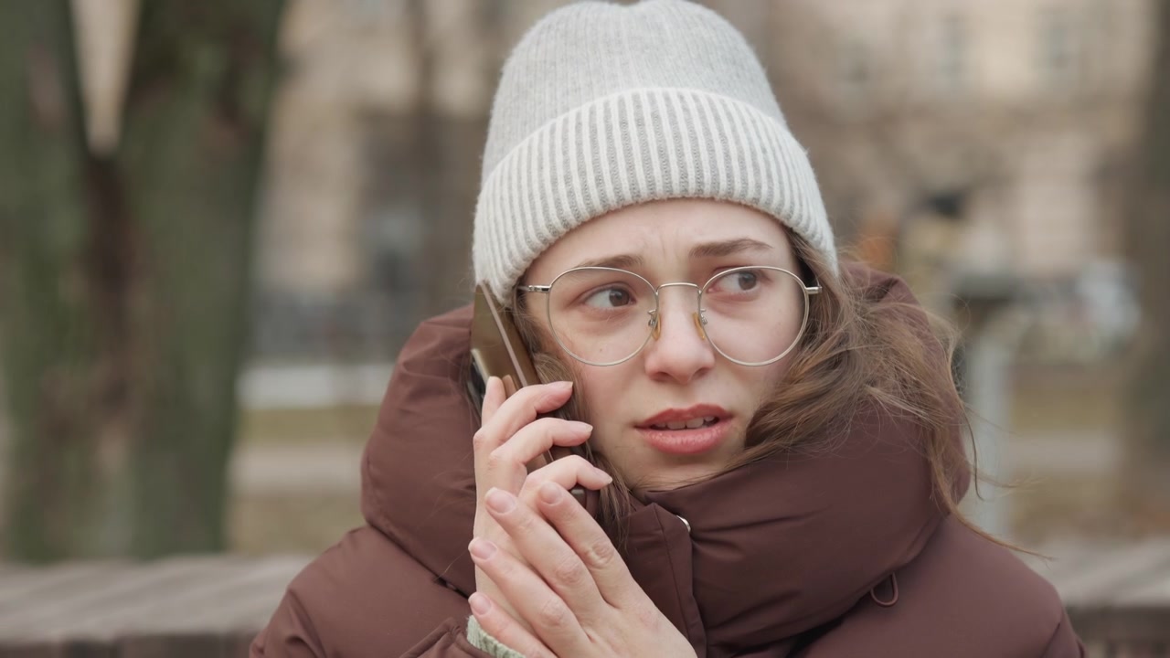 Park bankında acil telefon görüşmesi yapan Kafkas bir kadın arkadaş, canlı bir ifade ve yalvaran bir jest, kışlık ceket ve örgü şapka, ham duygu ve insan bağlantısıyla yakın bir konuşma çerçevesi.