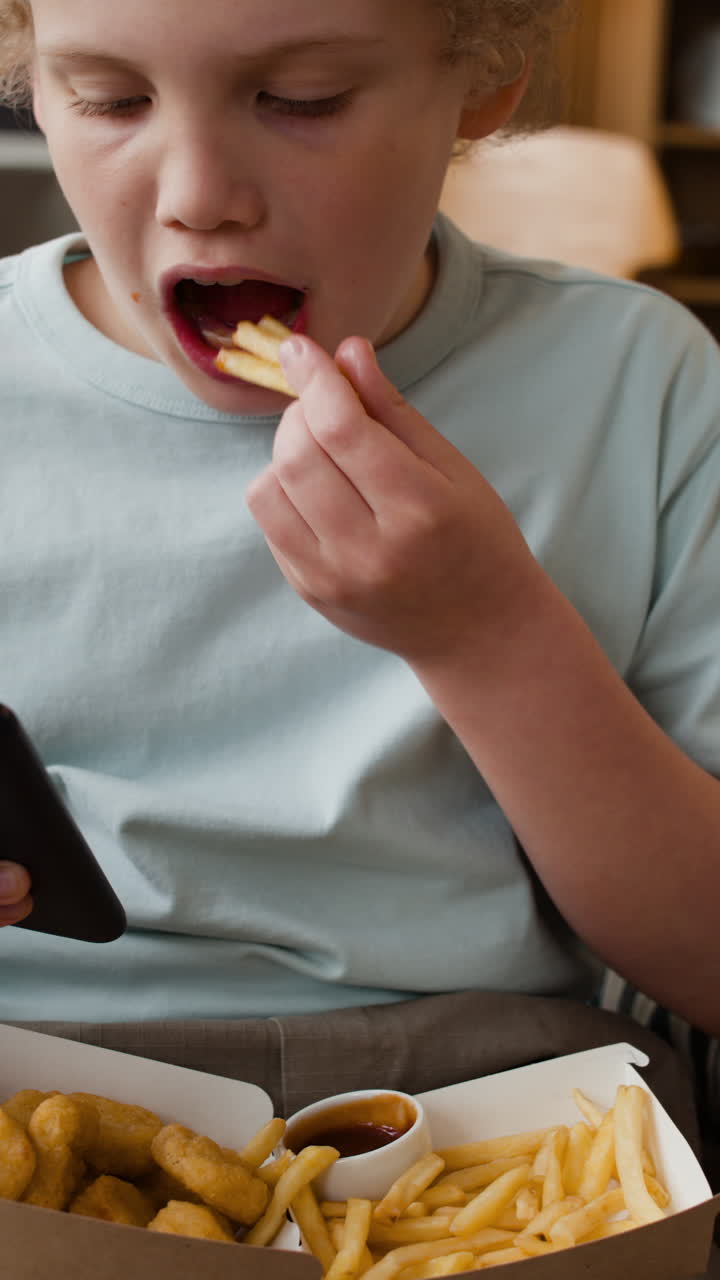Young boy eating fast food and looking at a smartphone