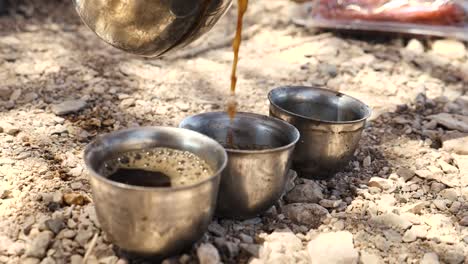 vista en ángulo bajo de tres tazas de metal para acampar en el suelo con café recién hecho vertido