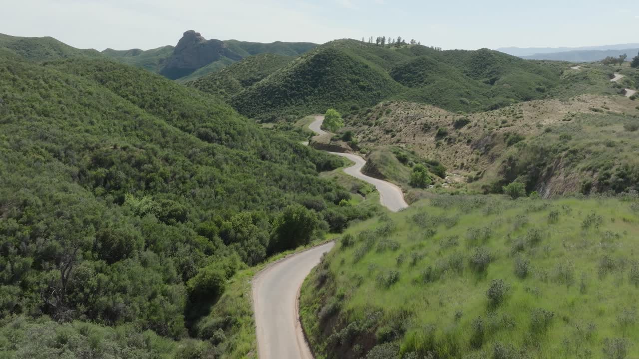 Aerial push-in shot of a lonely, winding curvy country road among lush rural green hills on a hazy sunny day in southern California.