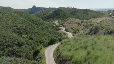 aerial push-in shot of a lonely, winding curvy country road among lush rural green hills on a hazy sunny day in southern california.