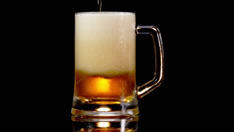 lager beer is poured into tankard mug, foamy white bubbles arise in black background