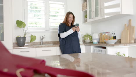 Happy-plus-size-biracial-female-doctor-with-coffee-using-smartphone-at-home,-copy-space,-slow-motion