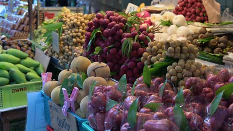 Frutas-Capturadas-Mientras-La-Cámara-Se-Desliza-Hacia-La-Izquierda-Mientras-Una-Mujer-No-Reconocida-Se-Mueve-Hacia-La-Izquierda,-Puesto-De-Frutas,-Tailandia