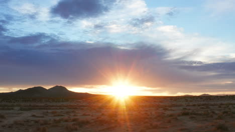 the sun flares over the horizon as dawn comes to the mojave desert's arid terrain - aerial sliding view