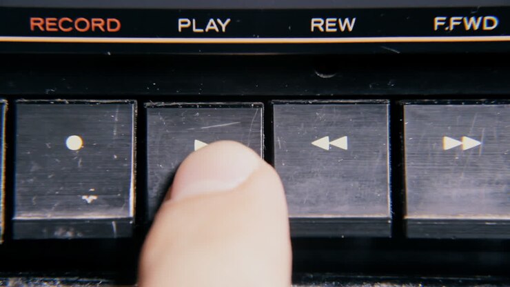 A finger pressing some buttons on an old retro vintage cassette tape player: play, rewind, fast forward, stop