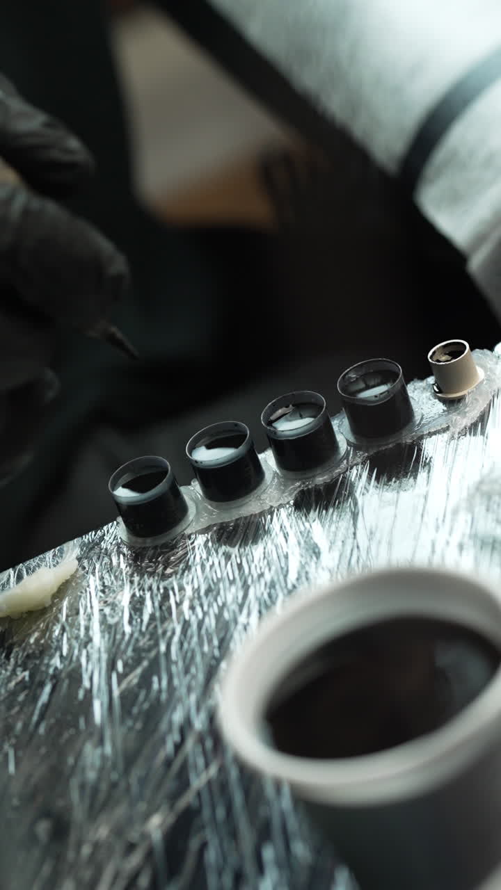 Close up vertical shot of a tattoo artist putting a needle in a small pot of black ink, interior