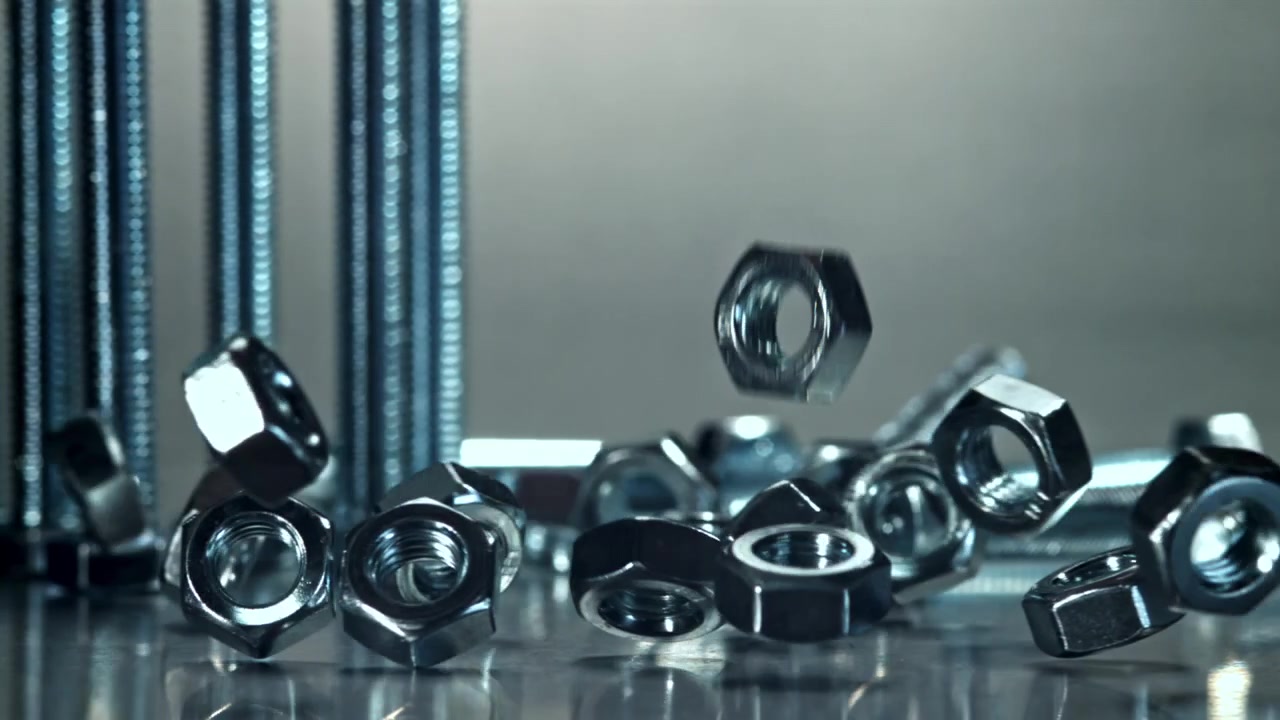 Metalmøtrikker falder i slowmotion ned på en reflekterende overflade