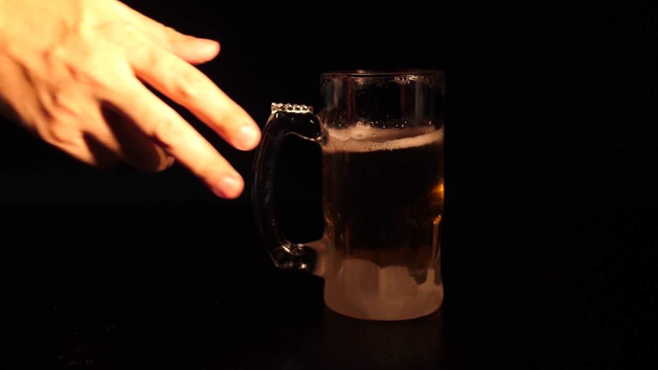 Una mano appoggia un boccale di birra brinato su sfondo scuro.