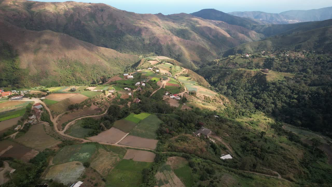 A winding road in a mountainous rural area surrounded by green fields, aerial view