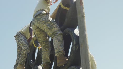 grupo diverso soldado masculino en uniforme de combate escalando la pared de neumáticos en la carrera de obstáculos del ejército en el sol