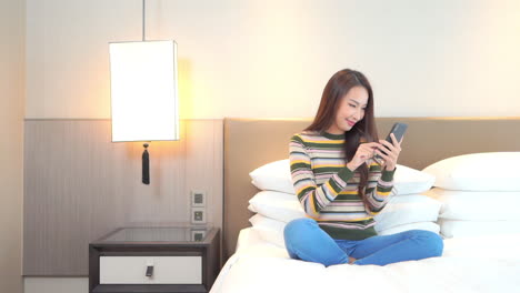 woman chats on smartphone while sitting with legs crossed on bed