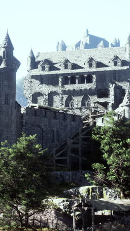 a majestic stone castle with towers and walls, surrounded by green trees and a wooden gate