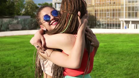 Two-happy-young-girls-with-dreads-hugging-each-other.-Excited-female-friends-embracing-each-other-and-laughing-during-the-sunny