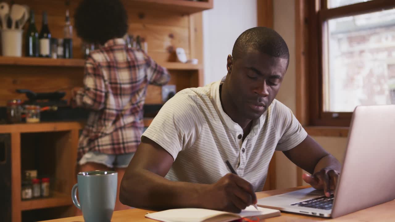 African man working while mixed race woman preparing breakfast