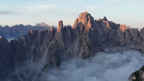 cinematic drone shot of cadini di misurina mountain covered by mysterious clouds at sunrise