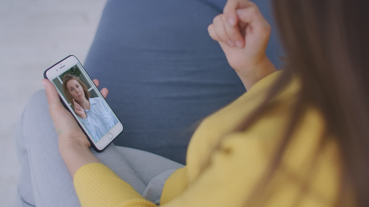mujer joven rizada que tiene una videochat con amigos usando la cámara del teléfono móvil mientras está acostada en la cama. mujer alegre atractiva sentada en el sofá y haciendo una videollamada con sus amigas