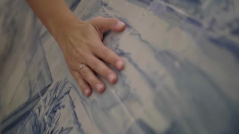 hand touching a wall of blue and white tiles