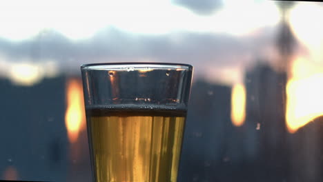 carbonation bubbles rise in short glass of pale lager beer by window